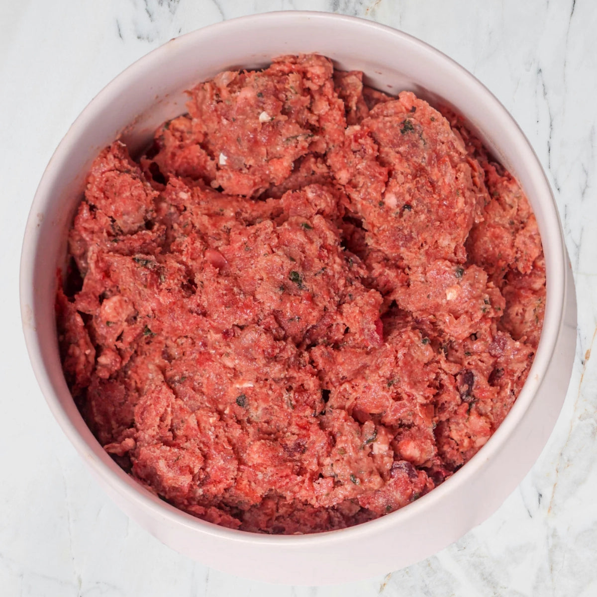 Pink bowl filled with raw dog food, ground meat on a light marble background