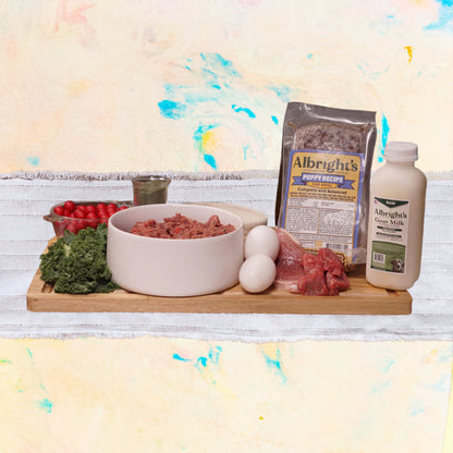 Raw dog food ingredients of Albright's pet food products on a wooden surface with a colorful abstract painting in the background.