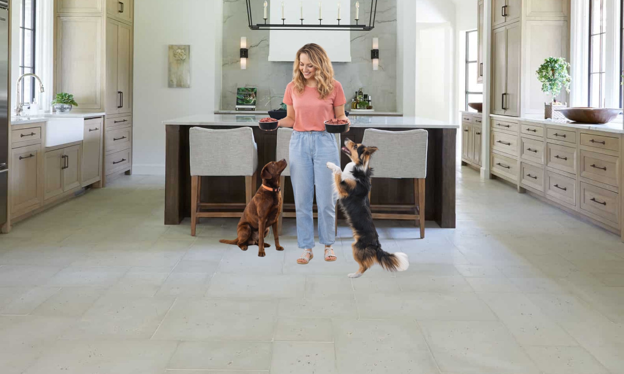 Woman standing in a modern kitchen with two dogs, holding a bowl.